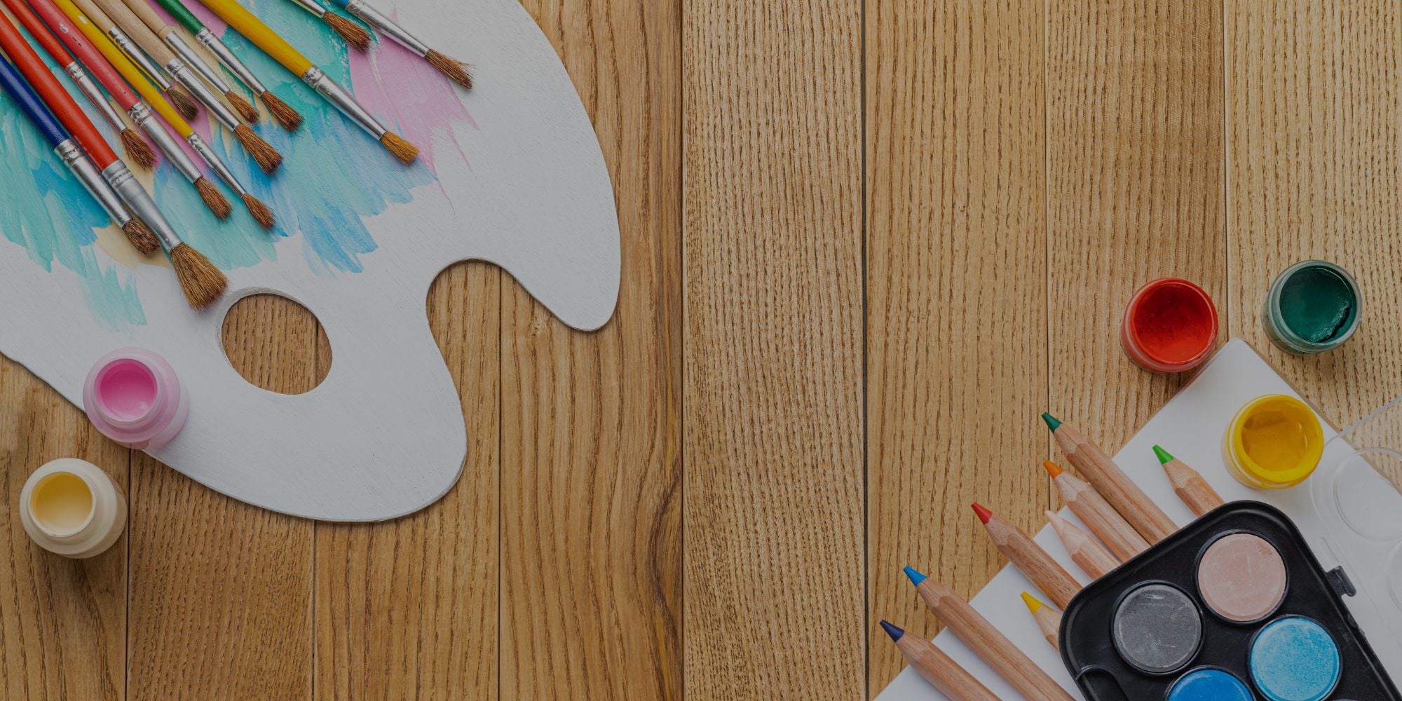 Art supplies including paintbrushes, paint containers, and a palette on a wooden surface.