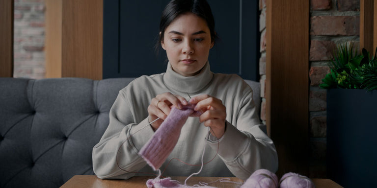 Woman knitting a pink item in a cozy living room.